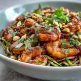 A close-up of a fresh Asian Noodle Bowl, featuring plump cooked shrimp, soft rice noodles, and crunchy vegetables, served with lime wedges for extra zest.