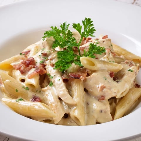 Hearty Creamy Chicken Bacon Penne served in a white bowl, garnished with fresh parsley and extra Parmesan alongside a glass of Chardonnay.