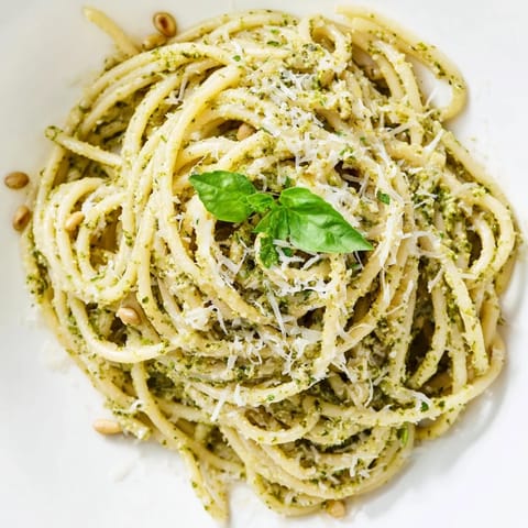 A warm plate of Creamy Sunflower Seed Pesto Pasta topped with extra Parmesan and fresh basil leaves, ready to eat.