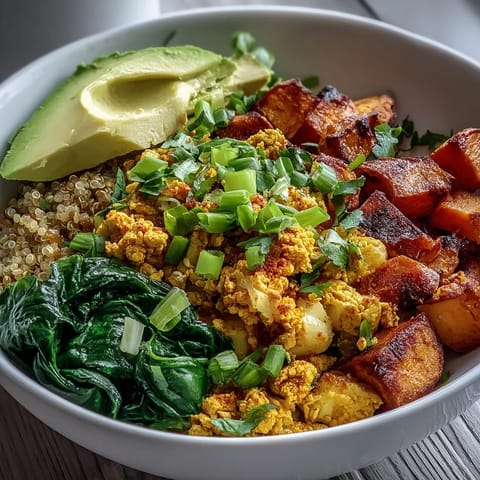 A vibrant vegan tofu scramble breakfast bowl with roasted sweet potatoes, sautéed spinach, fluffy quinoa, and creamy avocado slices.