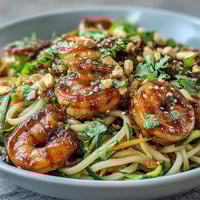 Vibrant Asian Noodle Bowl with tender shrimp, crisp julienned zucchini, and carrot tossed in a savory sesame-lime sauce, garnished with peanuts and fresh cilantro.