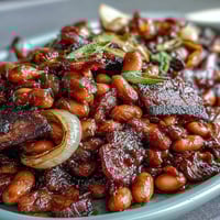 Summer BBQ baked beans with brown sugar and bacon in a cast iron skillet, topped with crispy bacon and bubbling sauce.